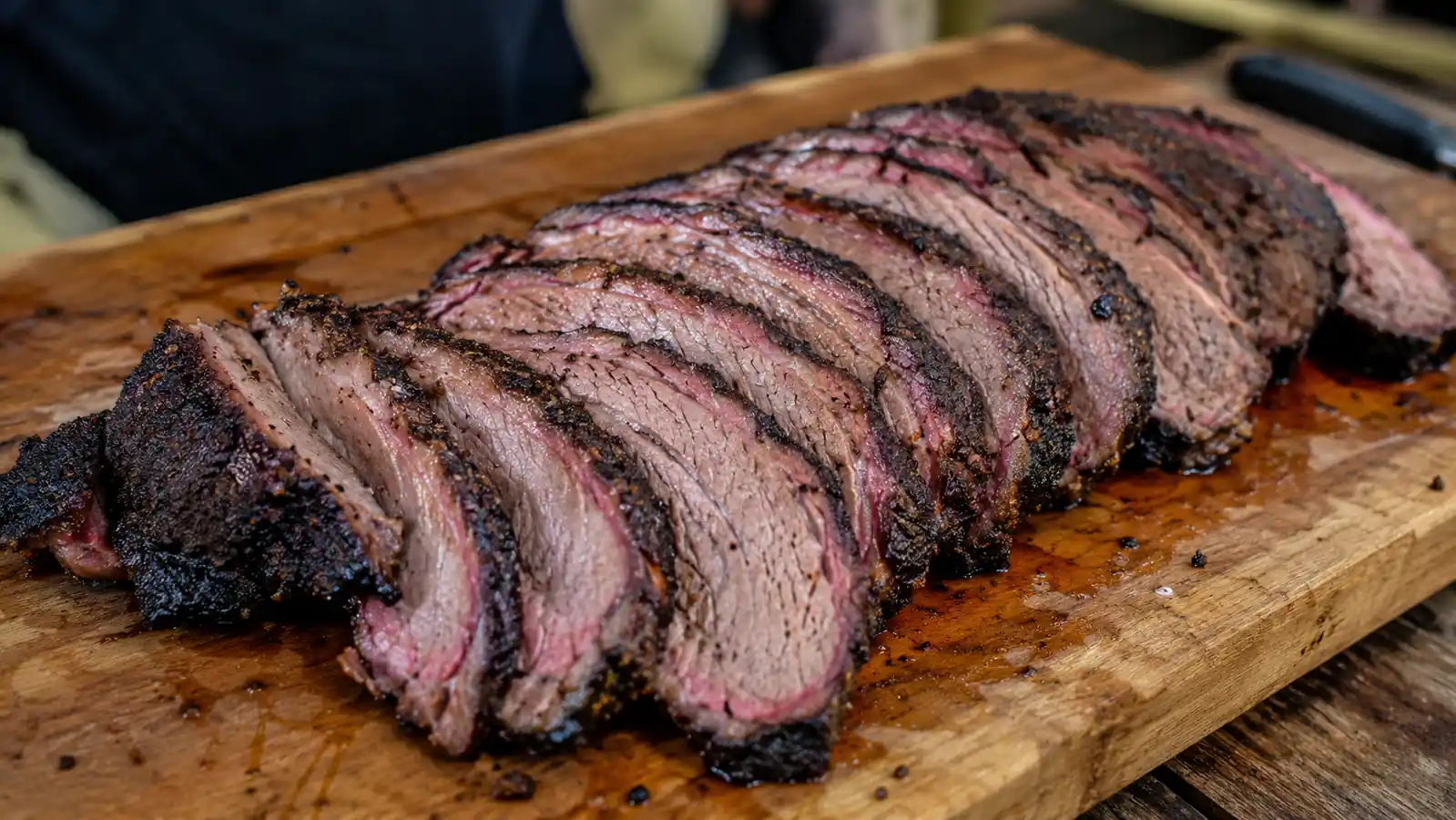 Sliced brisket on a cutting board showing a dark, cracked peppery bark and a smoke ring