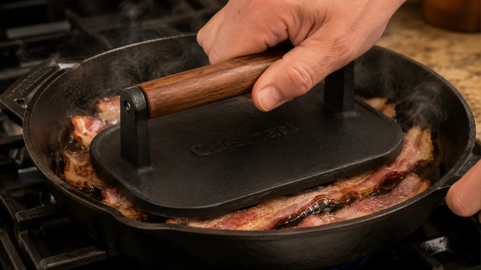 Hand pressing a cast iron grill press with wooden handle down onto strips of bacon in a skillet
