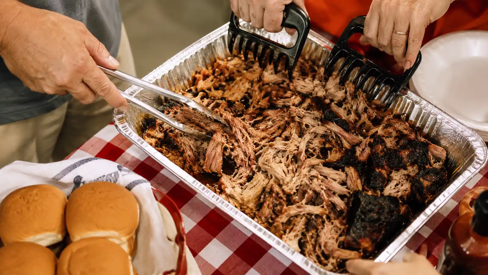 A full foil pan of finished pulled pork with claws resting on the edge, ready to serve