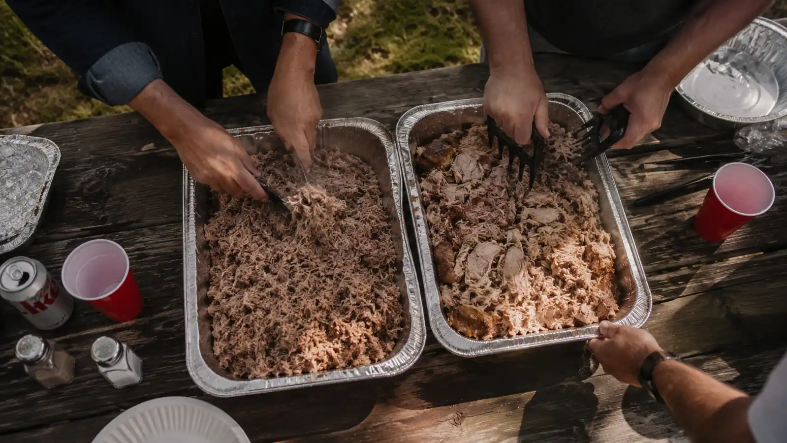 Two pork butts side by side on a cutting board, one shredded with claws and one with forks, showing the texture difference